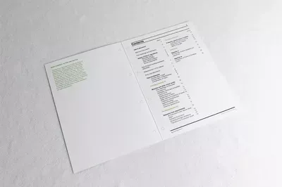 Printed LMC Christmas cards displayed as an open tri-fold design with minimalist layout featuring green text elements on white cardstock, photographed at an angle on a light background.