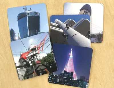 Four photographs arranged on a wooden surface featuring industrial and architectural subjects: a blue cylindrical storage tank, industrial piping and equipment, a red industrial crane or lifting mechanism, and an illuminated building at night.