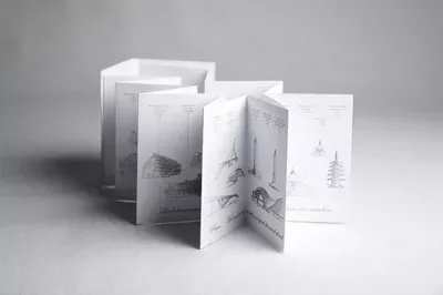 A folded white greeting card displayed open to reveal multiple interior pages with minimalist illustrations including winter trees and architectural sketches, shown alongside its packaging box.