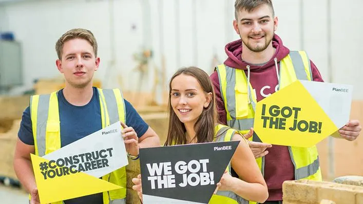 Three young people in high vis jackets from the PlanBEE programme hold up placards saying 